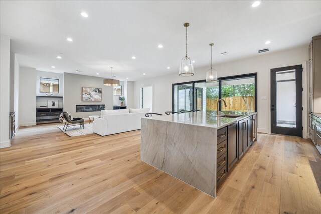 kitchen with light stone countertops, a center island with sink, recessed lighting, a sink, and light wood finished floors