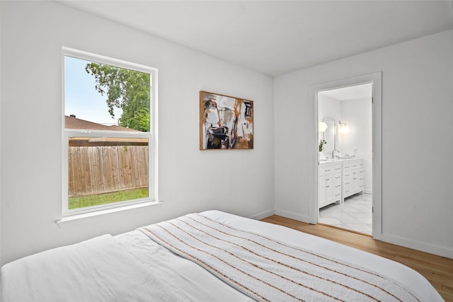 bedroom featuring baseboards, a sink, light wood finished floors, and connected bathroom