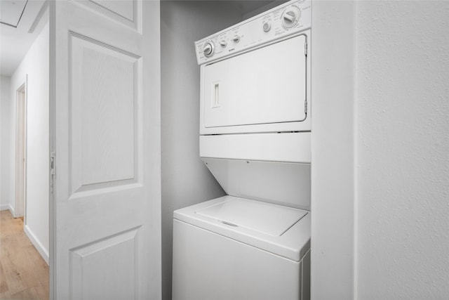 washroom with stacked washer and dryer, laundry area, baseboards, and light wood finished floors