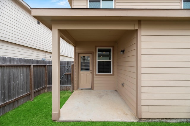 view of exterior entry with fence, a lawn, and a patio area