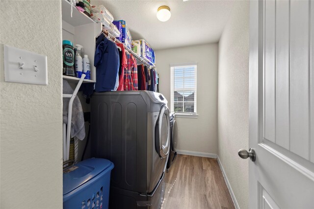 washroom featuring washing machine and clothes dryer, laundry area, a textured wall, baseboards, and wood finished floors
