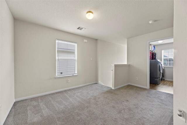 spare room featuring a textured ceiling, visible vents, baseboards, washer / dryer, and carpet flooring