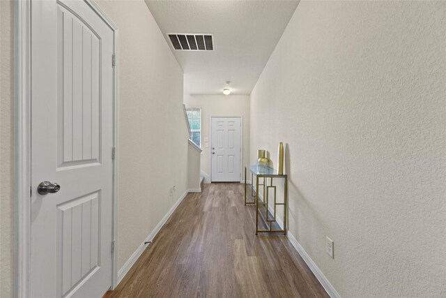 hallway with baseboards, visible vents, a textured wall, and wood finished floors