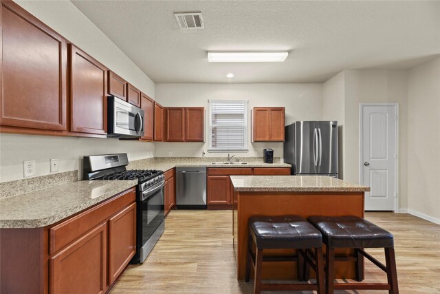 kitchen featuring visible vents, a breakfast bar, a sink, light wood-style flooring, and stainless steel appliances