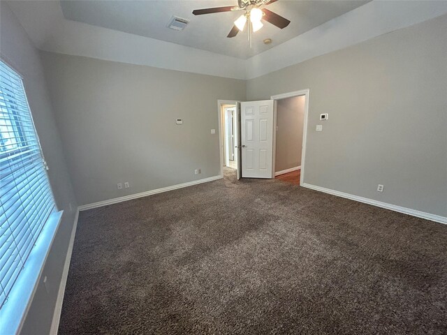 unfurnished bedroom featuring visible vents, baseboards, dark carpet, and ceiling fan