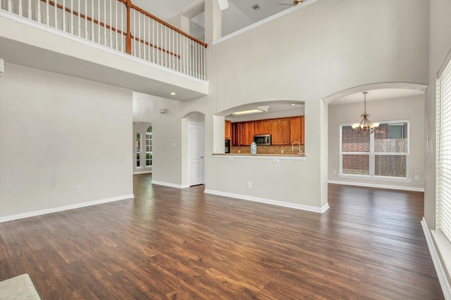 unfurnished living room featuring a notable chandelier, a sink, baseboards, a towering ceiling, and dark wood-style floors