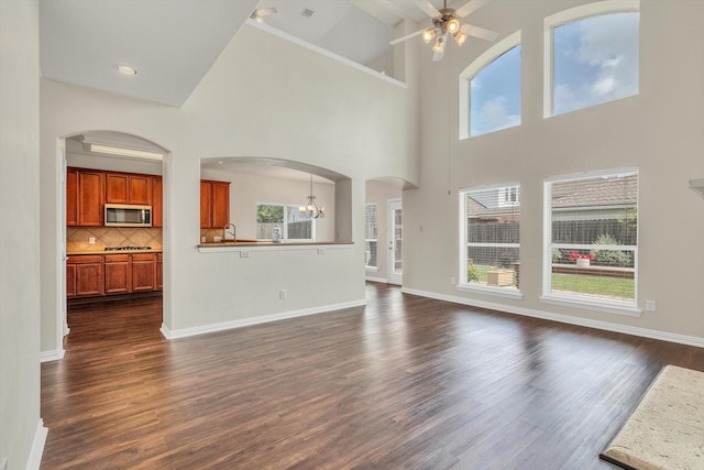 unfurnished living room with dark wood-type flooring, baseboards, ceiling fan with notable chandelier, and a high ceiling