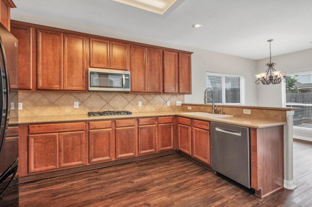 kitchen with an inviting chandelier, a peninsula, dark wood-type flooring, a sink, and stainless steel appliances