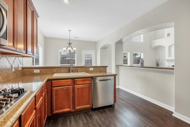 kitchen featuring a peninsula, baseboards, dark wood-type flooring, a sink, and appliances with stainless steel finishes