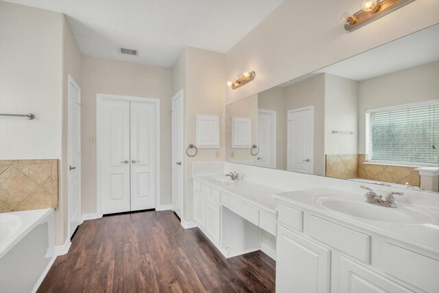 bathroom with a garden tub, visible vents, wood finished floors, a sink, and a closet