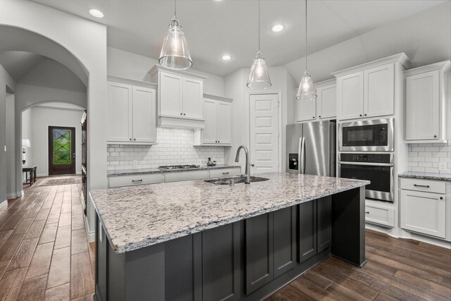 kitchen with appliances with stainless steel finishes, a sink, tasteful backsplash, a center island with sink, and dark wood-type flooring