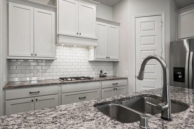 kitchen featuring a sink, stone countertops, stainless steel appliances, white cabinetry, and backsplash
