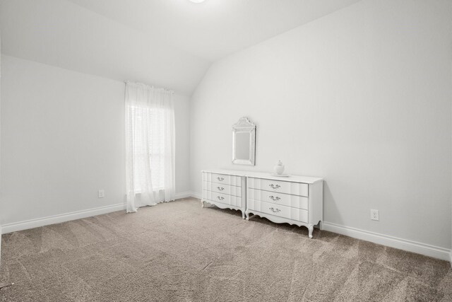 unfurnished bedroom with baseboards, lofted ceiling, and light carpet
