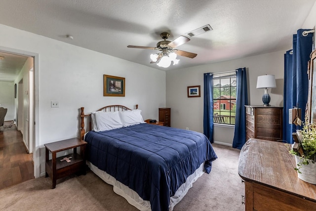 bedroom with visible vents, baseboards, ceiling fan, light colored carpet, and a textured ceiling