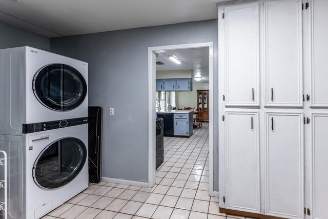 washroom with light tile patterned floors, baseboards, stacked washer and clothes dryer, and cabinet space