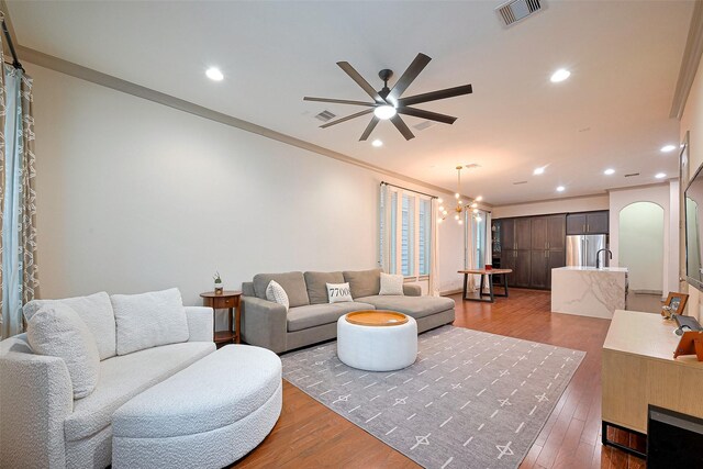 living room featuring arched walkways, visible vents, wood finished floors, and ceiling fan with notable chandelier