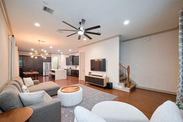 living room with ornamental molding, dark wood-style flooring, stairway, recessed lighting, and ceiling fan with notable chandelier