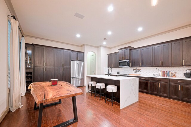 kitchen featuring dark brown cabinetry, backsplash, a center island with sink, a breakfast bar, and stainless steel appliances
