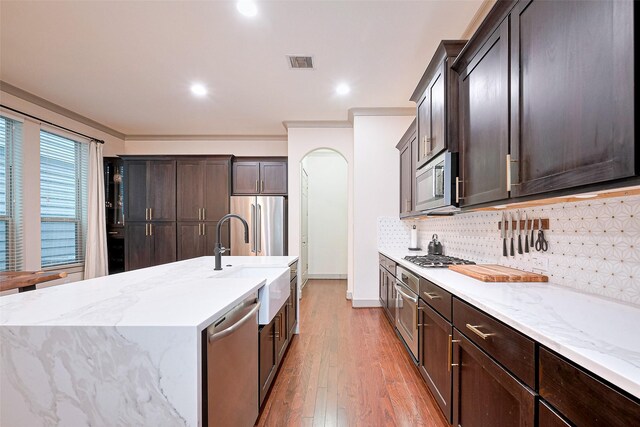 kitchen with dark brown cabinets, appliances with stainless steel finishes, a sink, light wood finished floors, and visible vents