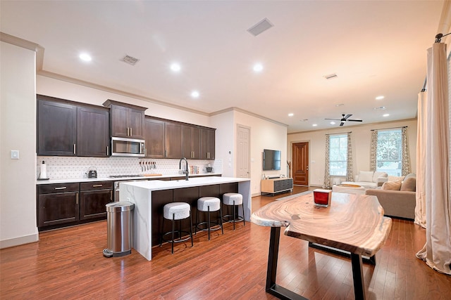 1224 Nelson Falls Ln, Houston, TX 77008 - kitchen featuring stainless steel microwave, a kitchen island with sink, backsplash, wood finished floors, and dark brown cabinets