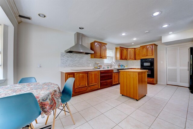 kitchen featuring a kitchen island, wall chimney range hood, recessed lighting, light countertops, and backsplash