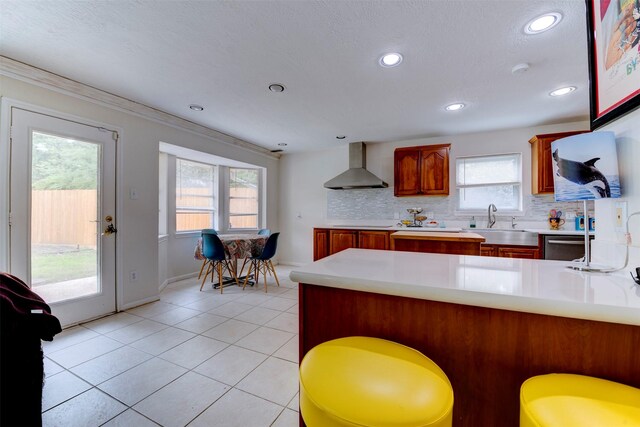 kitchen featuring tasteful backsplash, a sink, light countertops, a peninsula, and wall chimney exhaust hood
