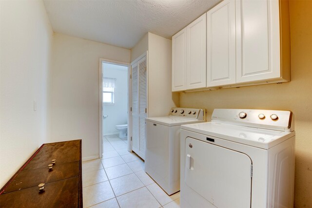 clothes washing area featuring separate washer and dryer, a textured ceiling, cabinet space, and light tile patterned floors