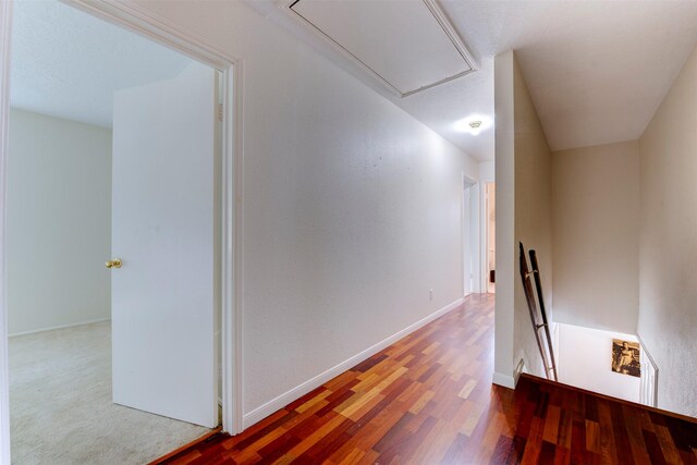 corridor featuring baseboards, attic access, wood finished floors, and an upstairs landing