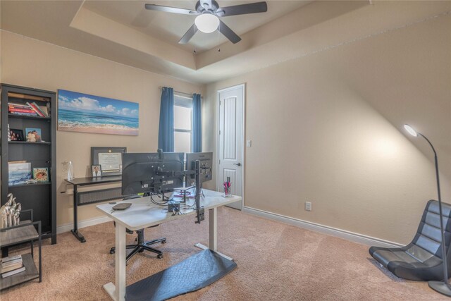 office space featuring a raised ceiling, a ceiling fan, baseboards, and carpet