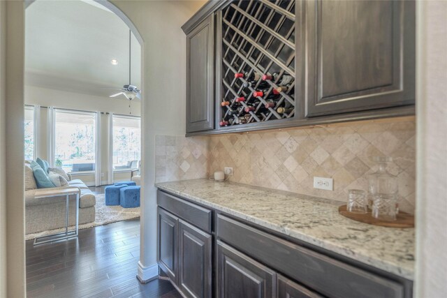 interior space with a ceiling fan, backsplash, arched walkways, a dry bar, and dark wood-style floors