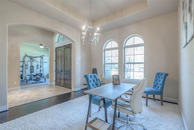 office area featuring arched walkways, baseboard heating, wood finished floors, baseboards, and a raised ceiling