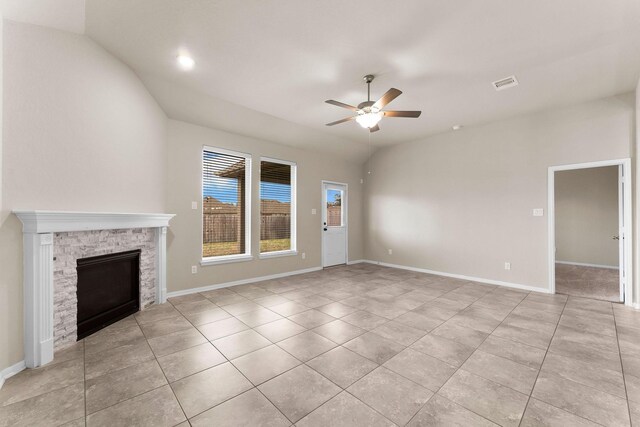 unfurnished living room with ceiling fan, a stone fireplace, visible vents, light tile patterned floors, and baseboards