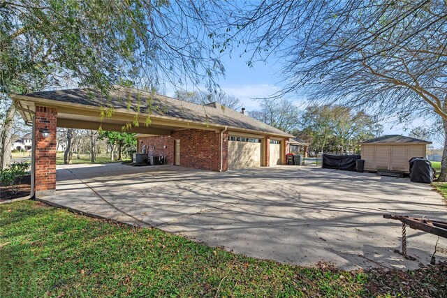 exterior space featuring a storage unit, an attached garage, brick siding, an outdoor structure, and driveway