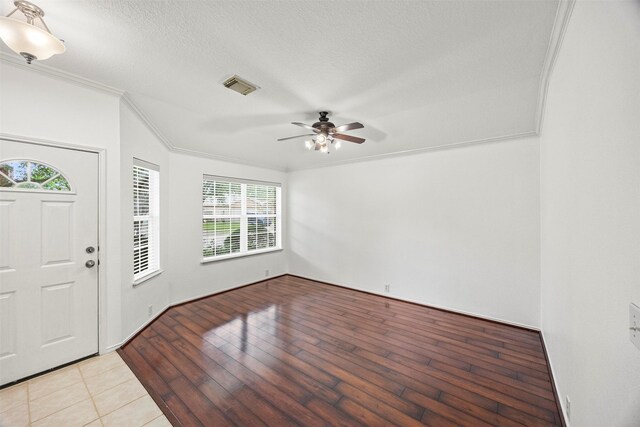 foyer entrance featuring ceiling fan, a textured ceiling, light wood-type flooring, visible vents, and ornamental molding