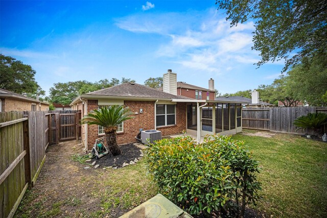 back of house with brick siding, a sunroom, a fenced backyard, central air condition unit, and a yard