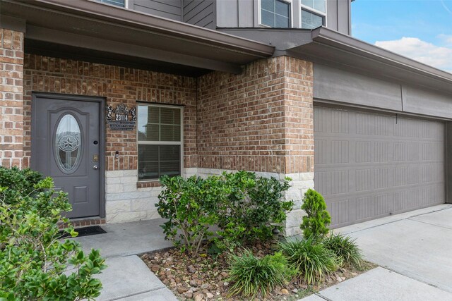 view of exterior entry featuring brick siding, an attached garage, and driveway