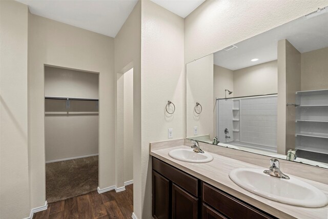 bathroom featuring double vanity, a walk in closet, a sink, and wood finished floors
