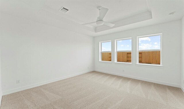 spare room with light colored carpet, a tray ceiling, visible vents, and baseboards