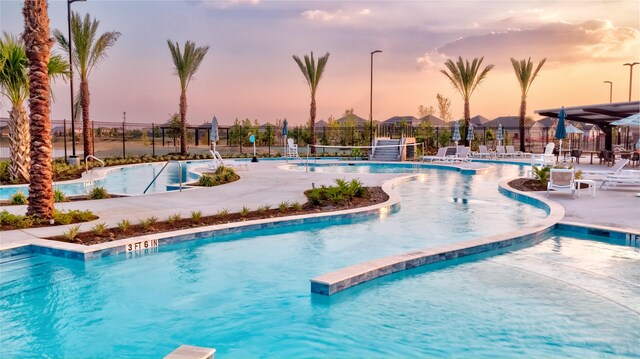 pool at dusk featuring fence, a community pool, and a patio area