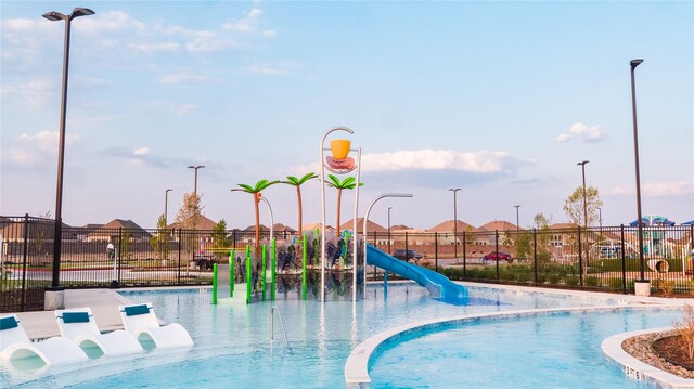 community pool with a water play area, a water slide, playground community, and fence