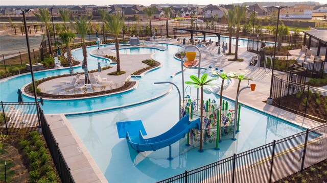 community pool with fence, a water slide, a water play area, and a residential view