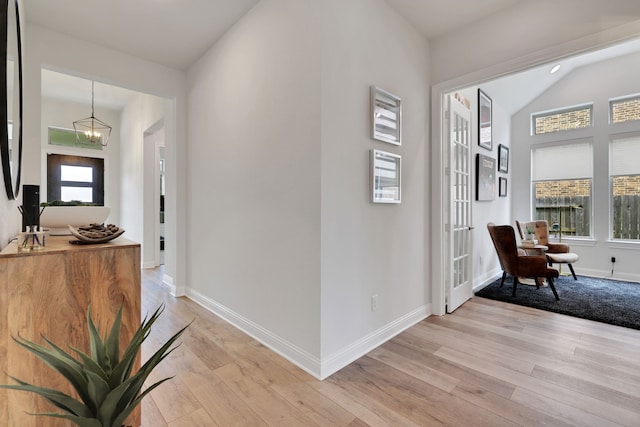 hall with baseboards, an inviting chandelier, a healthy amount of sunlight, and light wood finished floors