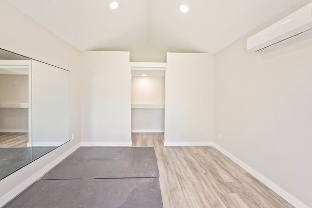 interior space with vaulted ceiling, wood finished floors, baseboards, an AC wall unit, and recessed lighting