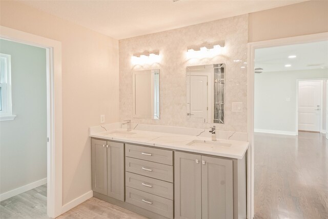 full bathroom with a sink, baseboards, double vanity, and wood finished floors