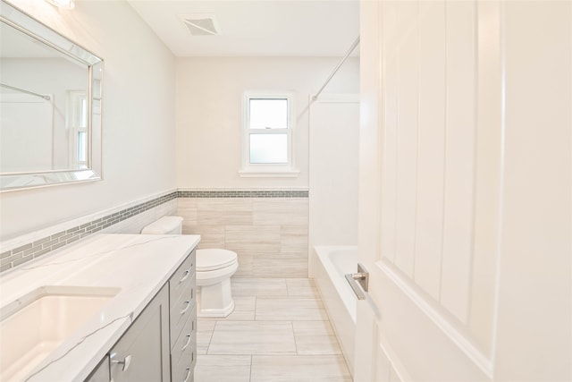 full bathroom featuring wainscoting, vanity, toilet, tile walls, and visible vents