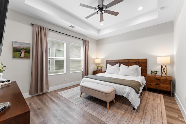 bedroom with visible vents, baseboards, light wood-type flooring, recessed lighting, and a raised ceiling