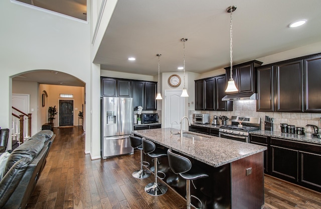 7610 River Pass Dr, Pearland, TX 77581 - kitchen with arched walkways, light stone countertops, a center island with sink, a sink, and stainless steel appliances