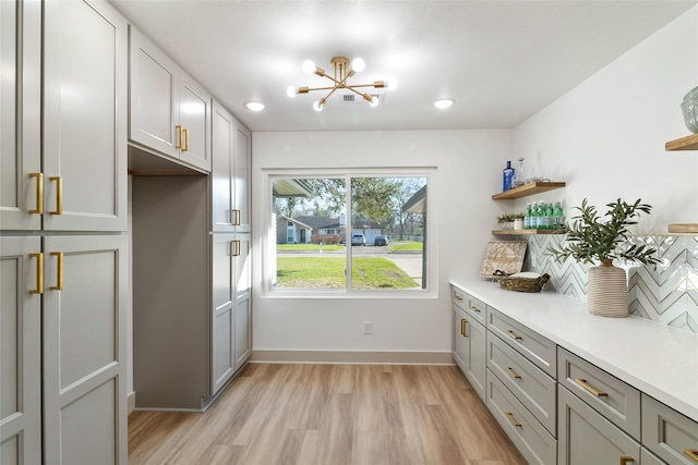 interior space with an inviting chandelier, light countertops, open shelves, and light wood-style flooring