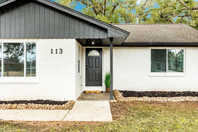 property entrance featuring brick siding and a shingled roof