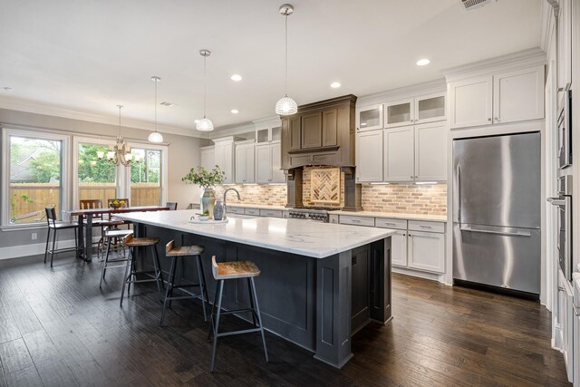 kitchen with appliances with stainless steel finishes, ornamental molding, backsplash, and an island with sink